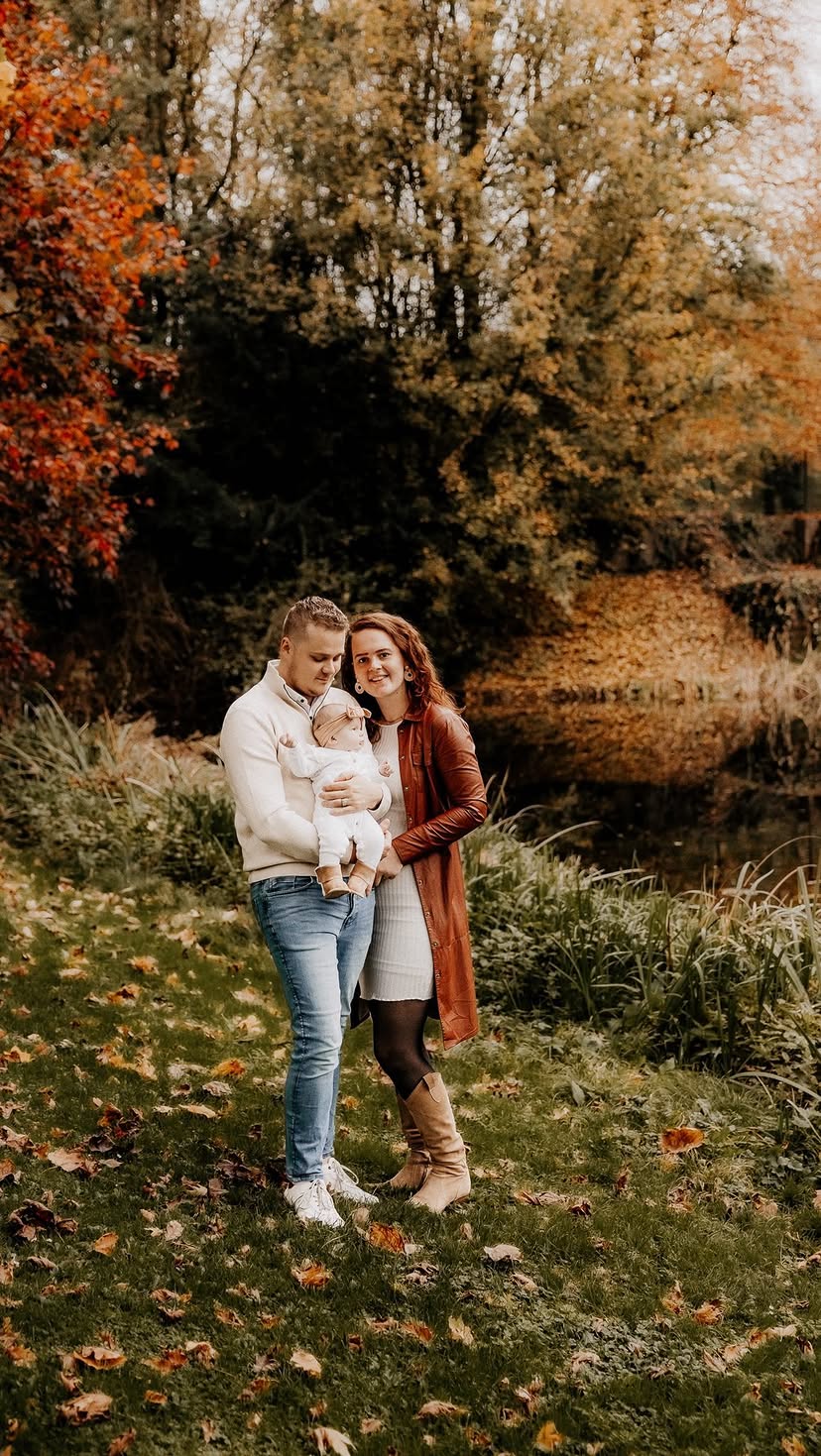 Jong gezin met baby aan de rand van een vijver tussen de herfstkleuren