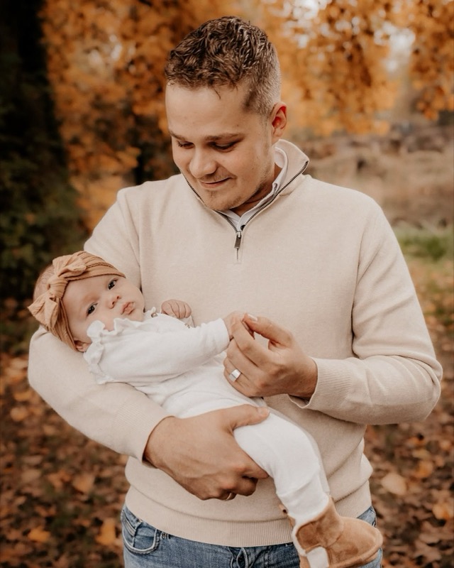Vader kijkt liefdevol naar zijn baby tussen oranje herfstbladeren