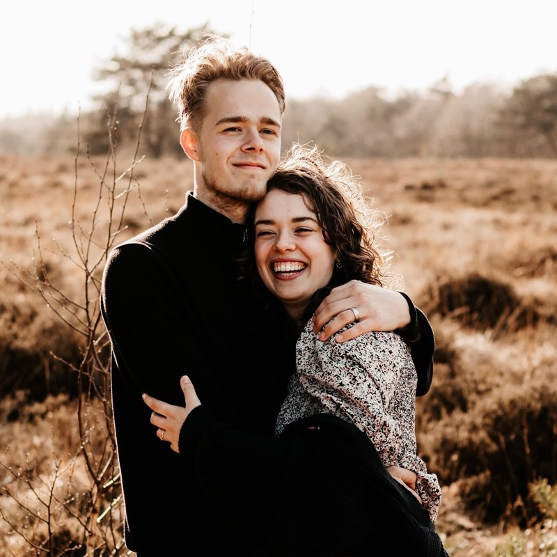 Verliefd stel omhelst elkaar lachend op de heide in warm tegenlicht
