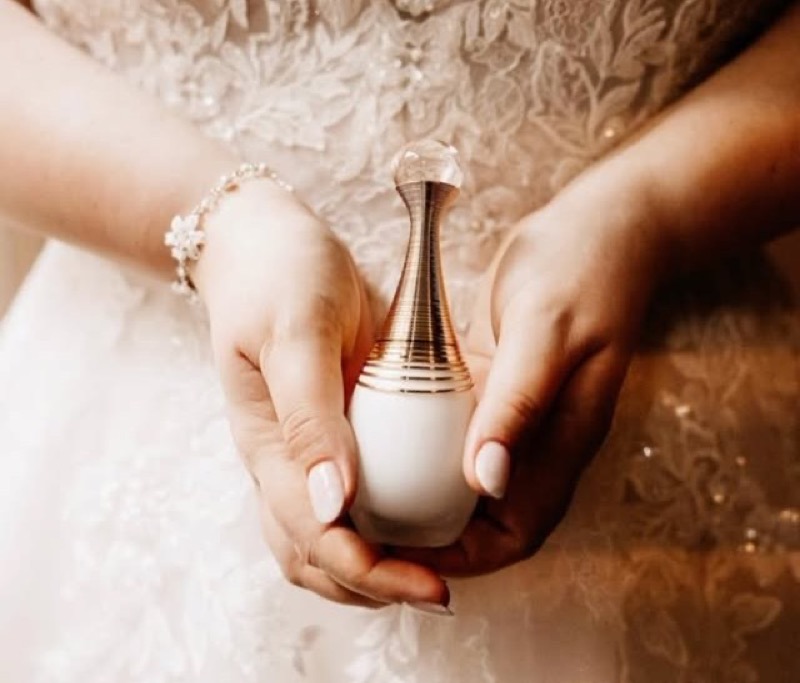 Handen van de bruid met een parfumflesje, kanten trouwjurk op de achtergrond